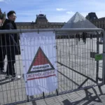 Tourist stand by a sign alerting on France’s Highest security level at Louvre Museum